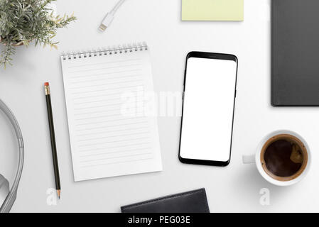 Empty notepad and modern smart phone mockup on white office desk surrounded with office supplies. Top view. Flat lay. Stock Photo