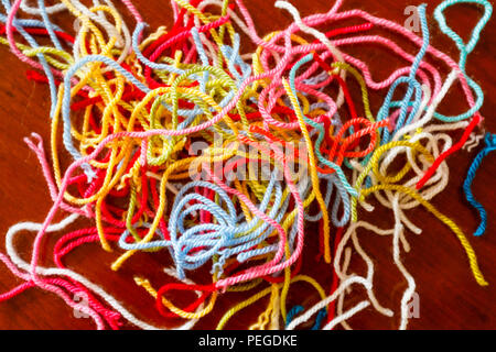 Abstract pattern: Colourful pile of left over lengths of pastel brightly coloured strands of wool offcuts used for home handicrafts on a wooden table Stock Photo