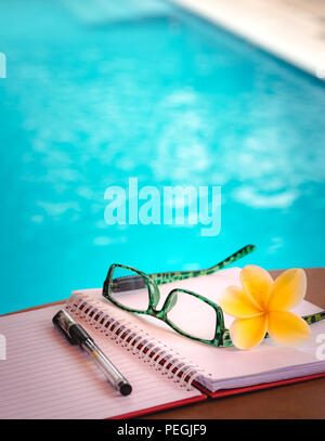 Open Book, Pen and Glasses on The Table Beside Swimming Pool. Working While on Vacation, Digital Nomad Concept Stock Photo