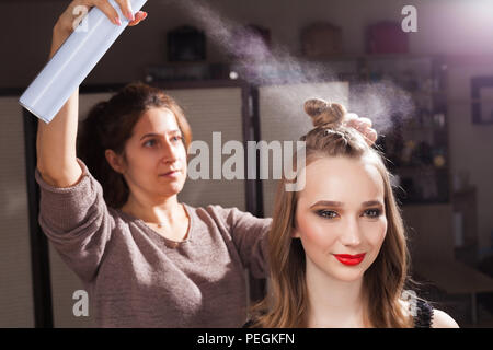 hairdresser fixing an unusual bun with a hair spray Stock Photo
