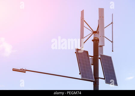 Wind turbine with solar panels on pillar against sky background. Public city light with solar panel powered on blue sky with clouds Stock Photo