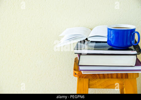 Stack of textbooks notepads workbooks blue cup of hot tea on high wooden stool on white wall background. University college education homeschooling le Stock Photo