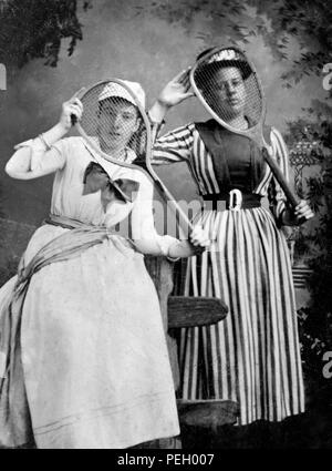 Two women in sporting clothes playfully pose with their tennis racquets in a late 19th century tintype image, ca. 1890. Stock Photo