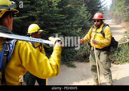 Second Lt. Julian Crockett, left, crew six leader, strike team two, Task Force First Round out of Joint Base Lewis-McChord, Wash., and Chris Scott, a military crew adviser tasked to provide oversight of Soldiers of Task Force First Round, brief their Soldiers on procedures they will use when putting in a fireline to help suppress the fire burning through Colville National Forest, Wash., Aug. 24, 2015. Crockett and Scott have taken the last week to learn about each other to increase the success of their mission. Stock Photo