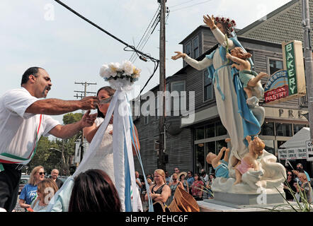 Cleveland, Ohio, USA.  15th Aug, 2018.  Final preparations are made on a float carrying the Holy Rosary Church Virgin Mary statue.  The float is part of a procession that will wind through the streets of this unique Cleveland Italian neighborhood in celebration of the 120th Feast of the Assumption.  A man pins money on the cloth, while baskets that are used for offerings are stacked on the float but will be used once the procession commences.  In the background is the Italy Bakery, Presti's, one of many Italian establishments in the area. Credit: Mark Kanning/Alamy Live News Stock Photo