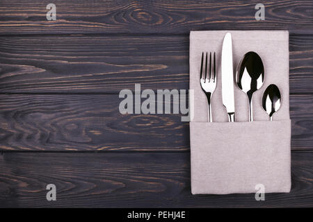 Set of fork, spoon, teaspoon and knife with linen napkin on wooden table. Top view. Stock Photo