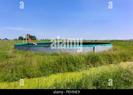 Vintage swimming pool made of an water storage reservoir with orange slide in the countryside pastures in the Netherlands Stock Photo