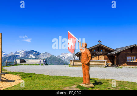 Wooden statue of a man holding a red and white cross Swiss national flag on Maennlichen, Jungfrau region above Wengen and Grindelwald, Switzerland Stock Photo