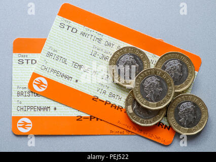 Two uk British rail railway train tickets with pound coins on top of them are pictured on a table top Stock Photo