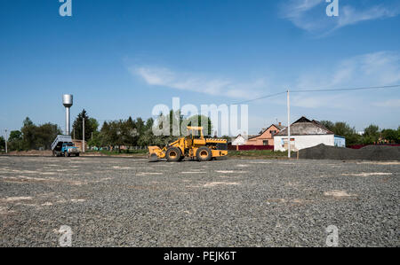 Yellow loader with empty bucket and blue truck standing on a stones at road construction and repairing asphalt pavement works. The stones for the road. Repaving Stock Photo