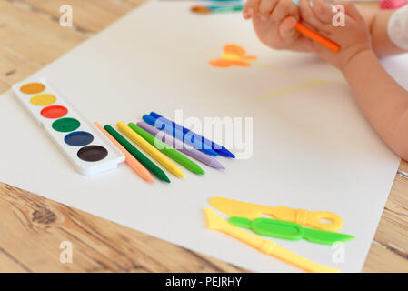 Little blonde girl painting on big white paper while laying on the floor indoors. Stock Photo