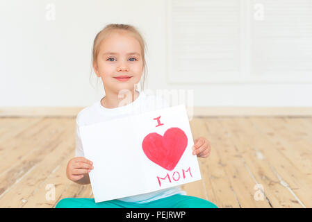 Little girl paints greeting card for Mom on Mother's Day with the inscription I love you mom . Indoors. Mother's Day concept. Stock Photo