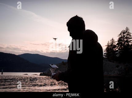 Silhouette of a man controlling a drone that is in the background. Stock Photo