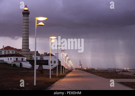 Pedestrian street along the sea of Leca da Palmeira in the evening seeing the lighthouse of Boa Nova and rain approaching Stock Photo