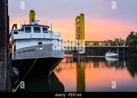 The Capitol Hornblower docked in Old Sacramento as the sun rises over the Tower Bridge and the Sacramento River in Sacramento, California. Stock Photo