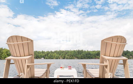 Muskoka chairs overlooking the lake with a bowl of cherries and a glass of champagne in between. Stock Photo