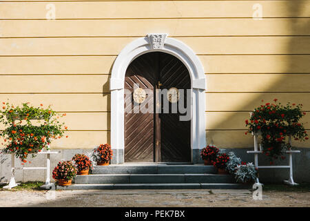 Beautiful arched doors with decorative elements and flower beds in sunny warm day Stock Photo