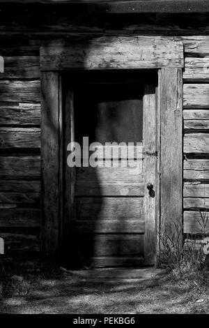 Cabin Door and Siding: Black and white photo, sunlight and shadows tease the weathered door in this early morning photo taken in a Montana ghost town. Stock Photo