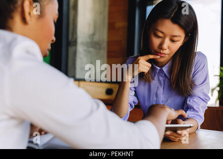 Two colleagues discussing new project, using digital tablet while sitting at table Stock Photo