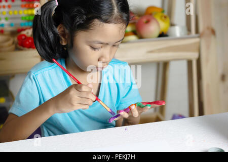 The little girl is painting color on finger with very concentrate. Select focus shallow depth of field with copy space. Stock Photo