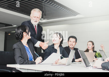 Explaining and discussing concept, Happy and kind manager talking  and praising with staffs by holding laptop and introducing his partners about manag Stock Photo
