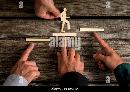 Business teamwork and cooperation concept with the hands of four businesspeople supporting paper cut outs of a man climbing the steps to success over  Stock Photo