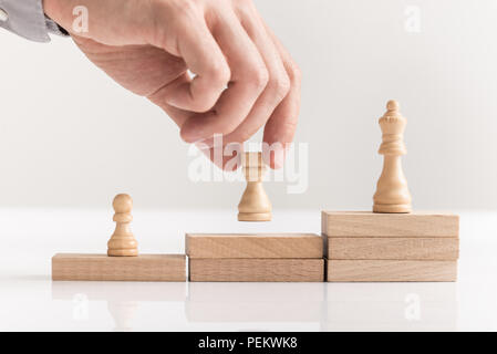 Businessman placing chess pieces on wooden blocks arranged as steps in a concept of corporate success in business, career and entrepreneurship in a cl Stock Photo