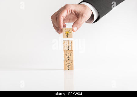 Illuminated light bulbs drawn on wooden blocks being placed on a white table by a businessman conceptual of bright ideas and success, with copy space. Stock Photo