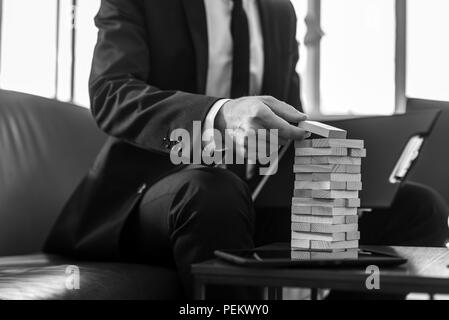 Man in business suit placing wooden domino in a tower, greyscale image. Conceptual of vision and planning. Stock Photo