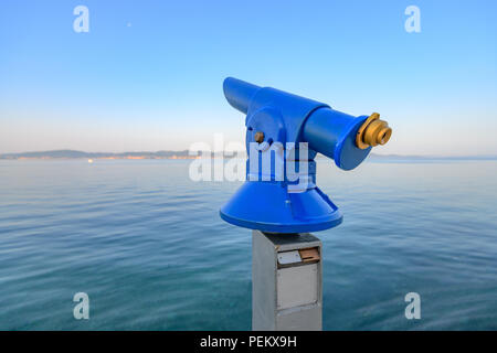 Blue public coin operated telescope, sea and island in background, located on waterfron early in the morning Stock Photo