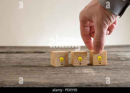 Illuminated light bulbs drawn on wooden blocks being placed on a rustic table by a businessman conceptual of bright ideas, inspiration, imagination, c Stock Photo