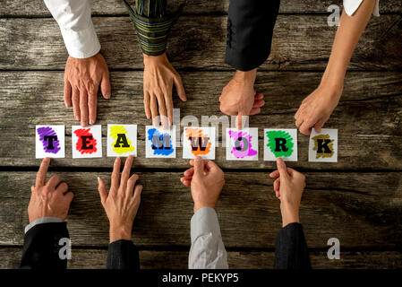 Top view of eight business people assembling the word TEAMWORK while each holding one colorful card with letter on it. Conceptual of cooperation and t Stock Photo