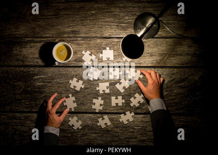Top view of male hands in elegant business suit trying to find a solution to a problem by arranging and matching puzzle pieces on a textured rustic wo Stock Photo