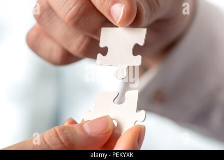 Two businesspeople fitting together matching interlocking puzzle pieces conceptual of teamwork and problem solving, closeup of their hands. Stock Photo