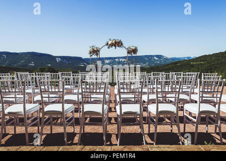 Beautiful decorated wedding ceremony outdoor with mountain view. A lot of white chairs and carved forged arch with flowers Stock Photo