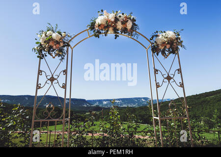 Beautiful decorated wedding ceremony outdoor with mountain view. A lot of white chairs and carved forged arch with flowers Stock Photo