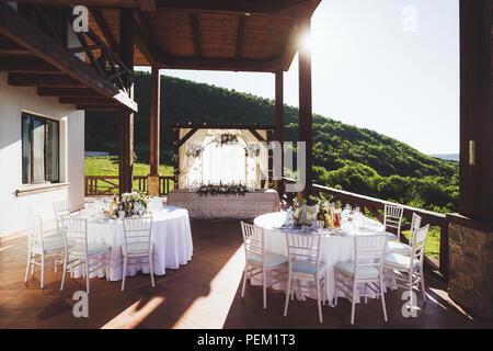 Beautiful decorated wedding ceremony outdoor with mountain view. A lot of white chairs and carved forged arch with flowers Stock Photo