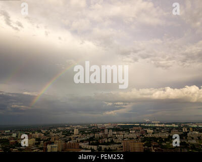 Two multicolored rainbows in the gray sky with clouds after the rain over the big city Stock Photo