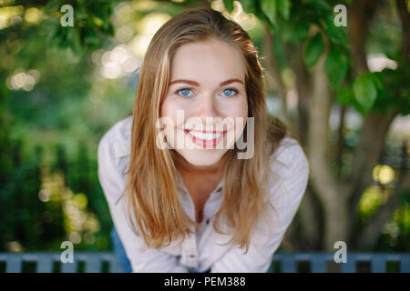 Closeup portrait of beautiful smiling white Caucasian girl woman with long blonde  hair and blue eyes, wearing white shirt and jeans, outside in summe Stock Photo