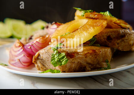 Marinated Cuban pineapple pork chops with traditional black bean rice grilled red onion and fried plantain chips Stock Photo