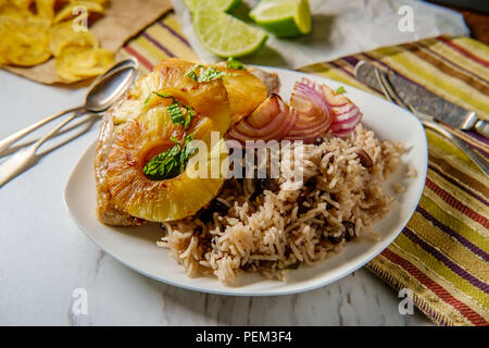 Marinated Cuban pineapple pork chops with traditional black bean rice grilled red onion and fried plantain chips Stock Photo