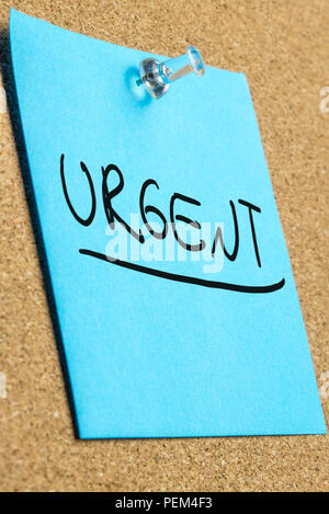 Blue post it paper pinned to a cork bulletin board with word Urgent written on it. Stock Photo
