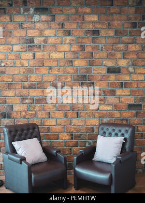 Loft interior concept. Two leather sofa and pillows on Brick wall background with copy space vertical style. Stock Photo