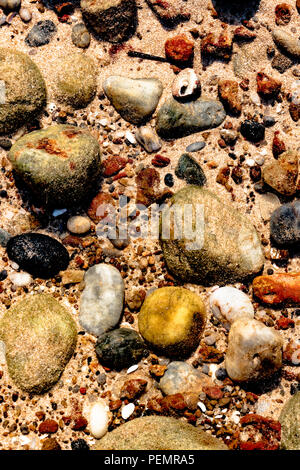 Beautiful colorful stones, sea shells and geological rocks containing minerals of sea lying underwater on the sea floor in the shallow waters. Stock Photo