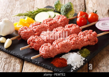 Homemade kebabs from raw minced meat on skewers with spices, herbs and vegetables close-up on the table. horizontal