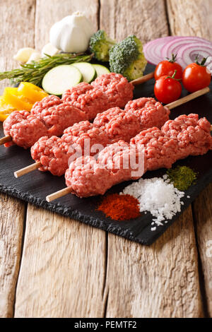 For roasting raw minced meat on skewers with the ingredients and vegetables close-up on the table. vertical Stock Photo