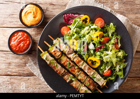 Delicious kebab on skewers with fresh vegetable salad on a plate and sauce close-up on the table. Horizontal top view from above Stock Photo