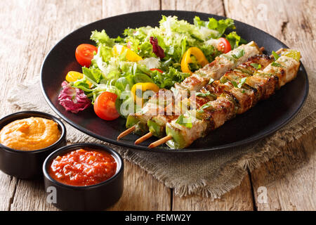 Freshly cooked kebabs with pepper on skewers with fresh salad on a black plate and ketchup and mustard close-up on the table. horizontal Stock Photo