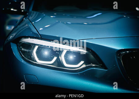 Car headlight and hood of powerful sports blue car with blue glare on dark background. Close up at Car headlight. Stock Photo