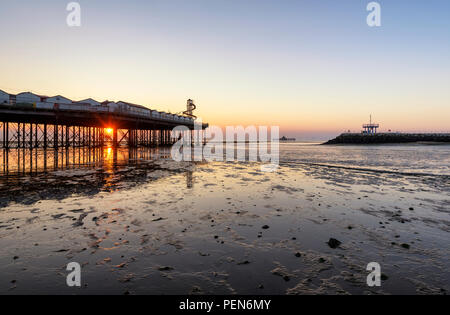 Sunset pokes through gaps in Herne Bay pier on the Kent coast. View of Herne Bay pier, Neptune's Arm and the Old Pier. Stock Photo